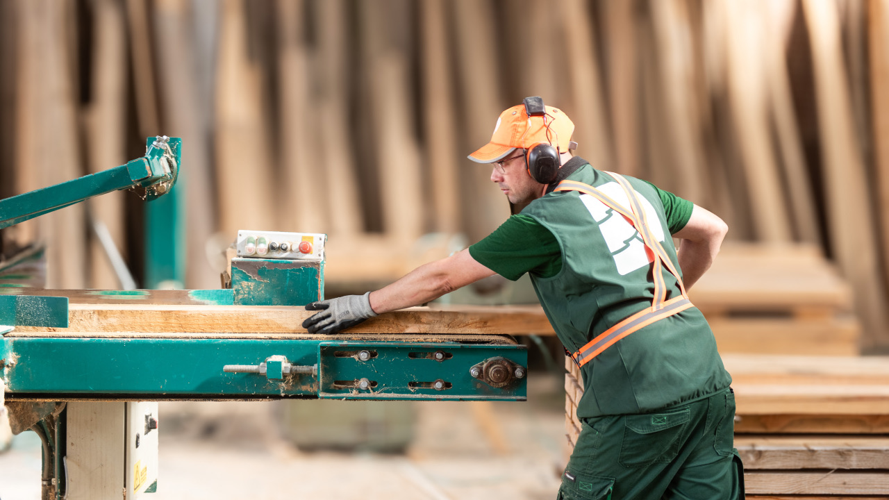 Employé de Denoyelle scierie vu de profil en train de raboter une planche de bois